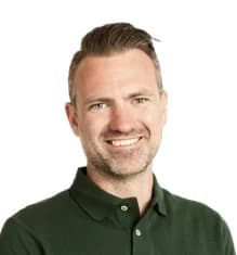Smiling man with short hair wearing a dark green collared shirt, against a white background.