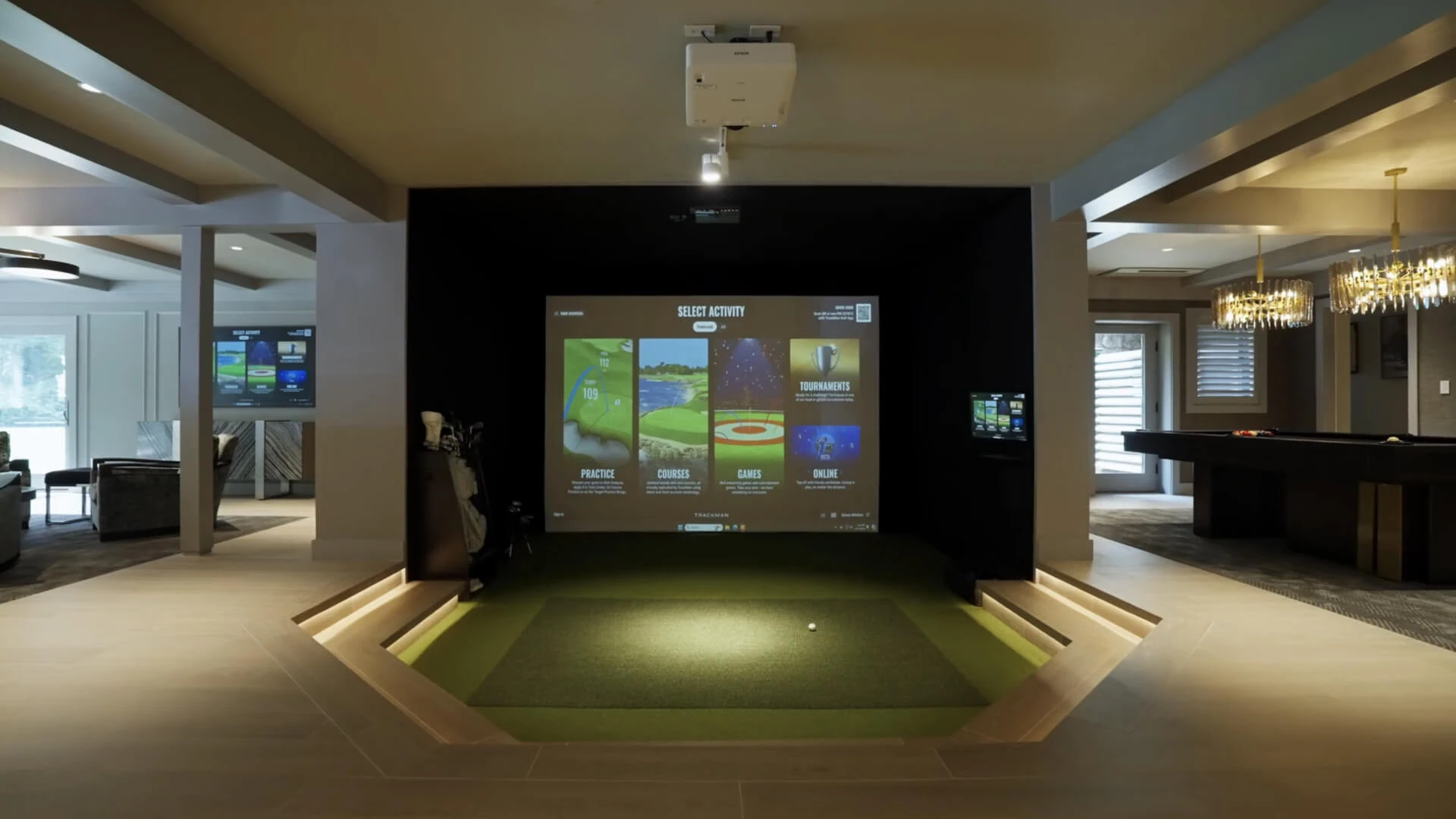 A modern indoor golf simulator setup in a spacious room with a large screen displaying a virtual golf course and golf equipment nearby.