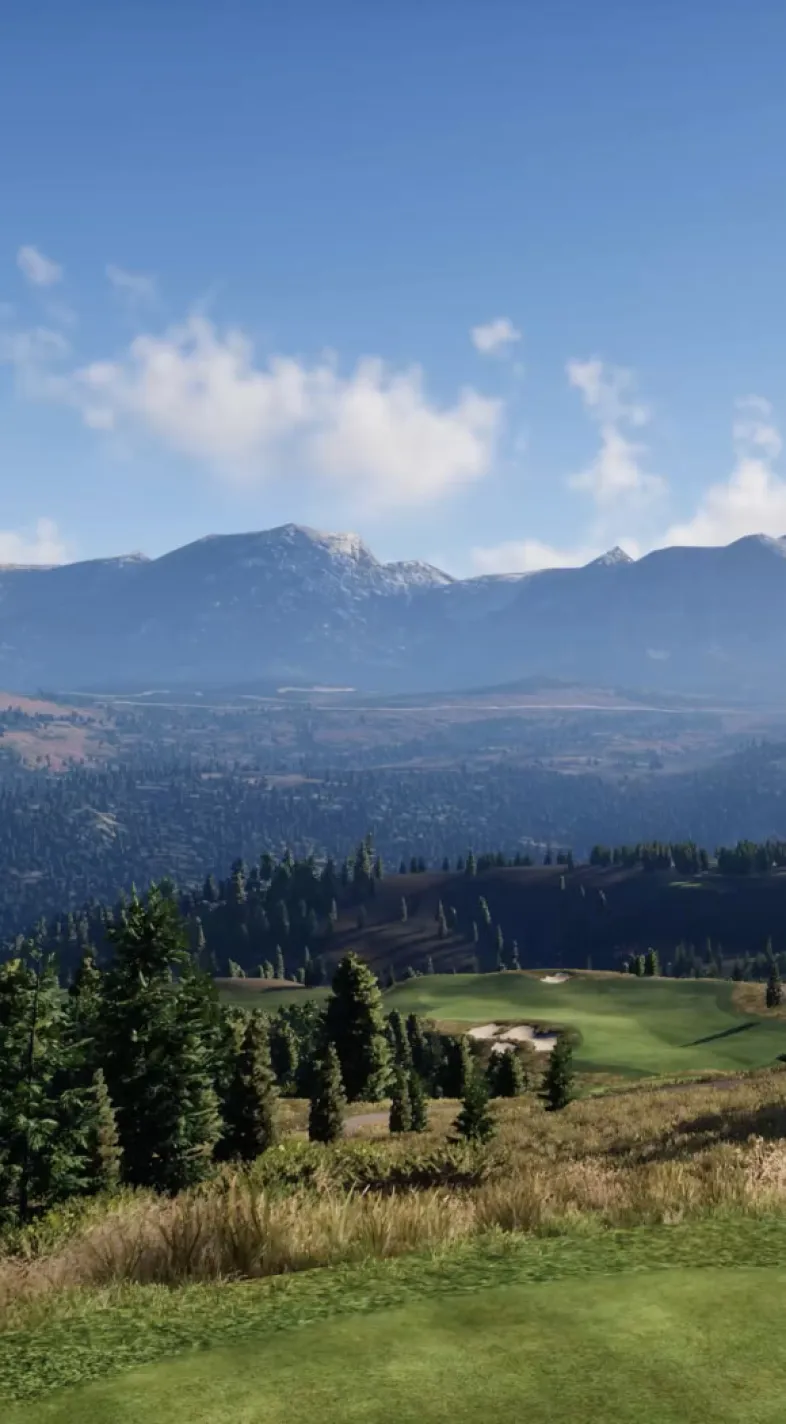 Mountain landscape with a clear blue sky, distant snow-capped peaks, and a lush green valley dotted with trees in the foreground.