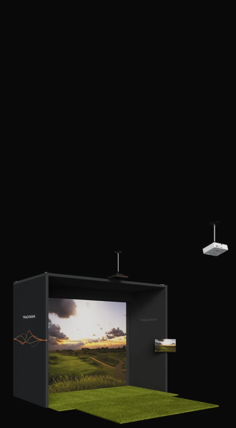 Golf simulator setup with a large screen displaying a golf course, surrounded by black walls and green turf flooring. Ceiling-mounted projector.