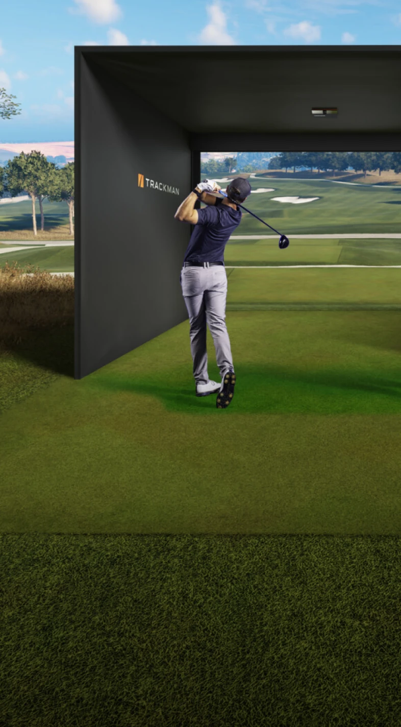Golfer in mid-swing on a green, using a golf simulator with a large screen displaying a golf course.